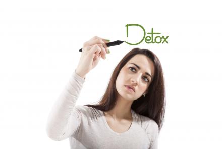A woman in white writing the word Detox on a board